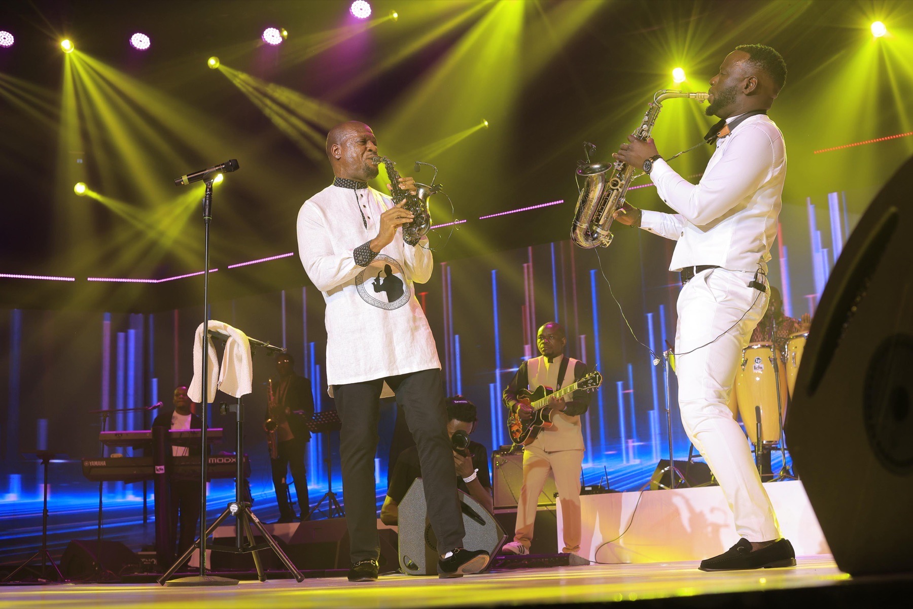 Two saxophonists performing together under yellow stage lights