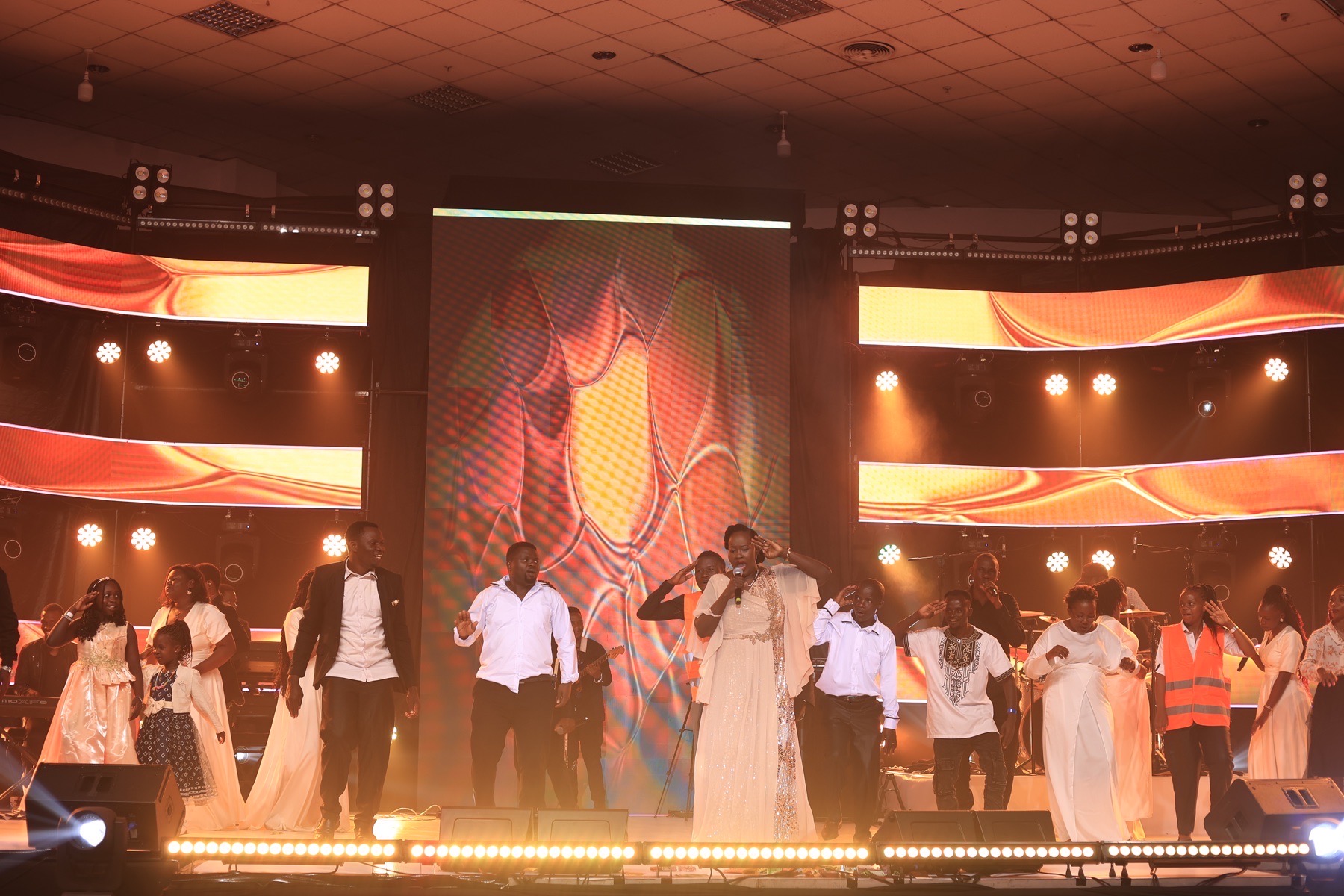 Choir and lead vocalist performing across a brightly lit stage