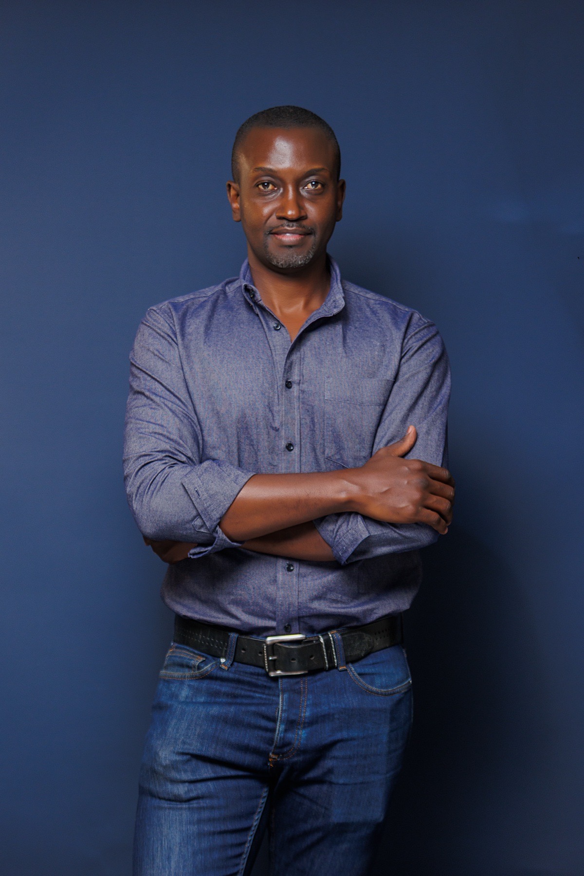 Man standing with folded arms against a blue studio backdrop